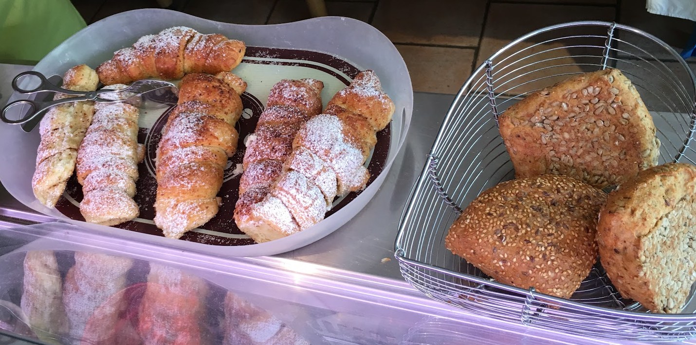 Theke mit Hörnchen unter Puderzucker und einem Drahtkorb voller Körnerbrötchen